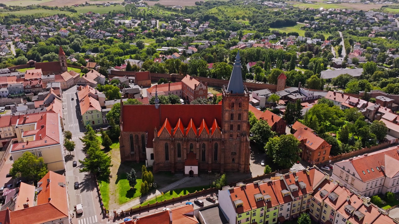 Drone orbits historic gothic church in Chełmno with rooftops and summer trees