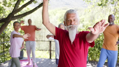 diverse senior male instructor and friends practicing yoga standing in sunny nature, slow motion