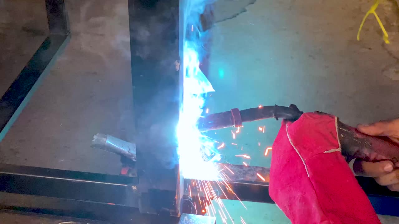 Close up shot of man hands wearing red welding gloves while doing welding process
