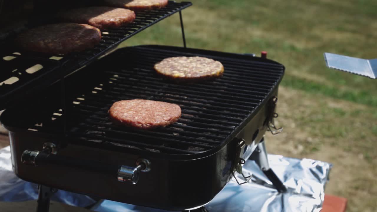 Mano di un uomo che apre la griglia e gira gli hamburger