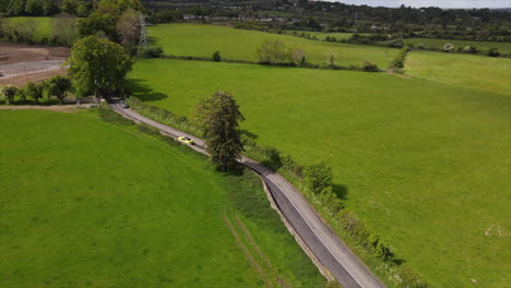 Bright-yellow-car-travels-along-Irish-countryside-road