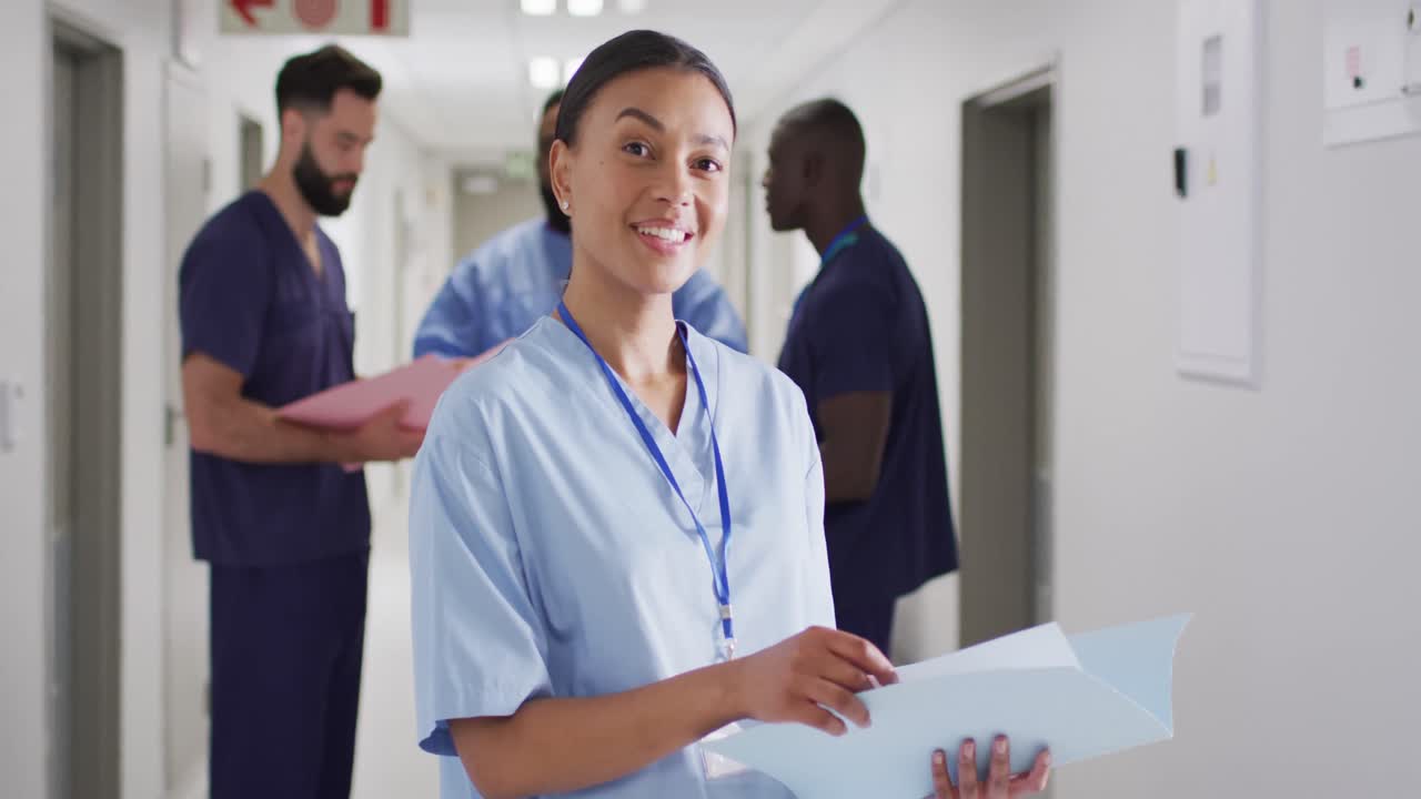 retrato de video de una trabajadora médica biracial sonriente en un concurrido pasillo del hospital