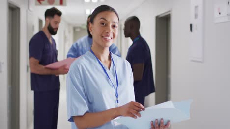 retrato de video de una trabajadora médica biracial sonriente en un concurrido pasillo del hospital