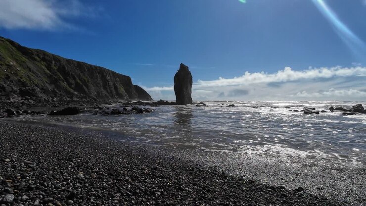 Maree piene con onde dolci e un imponente faraglione su una spiaggia di ciottoli a Ballydwane, Waterford, Irlanda.