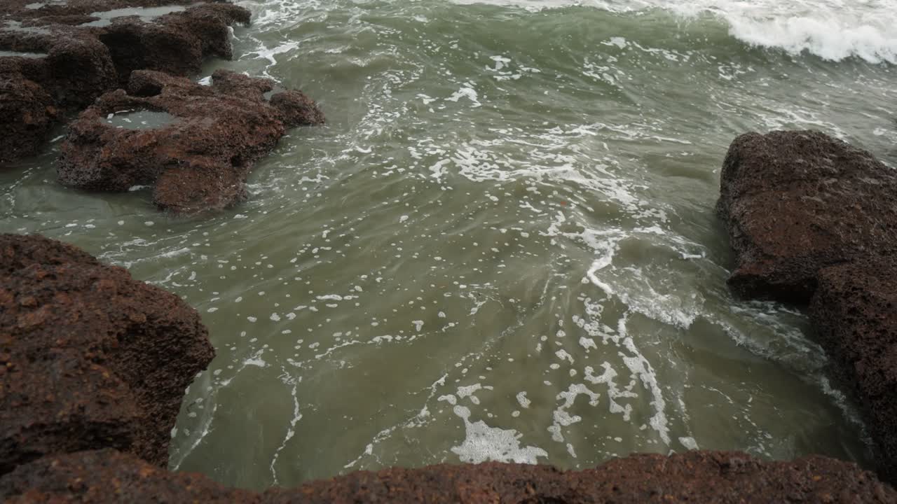 las olas chocan contra una costa rocosa en un día nublado, creando una interacción dinámica entre el agua y las rocas escarpadas
