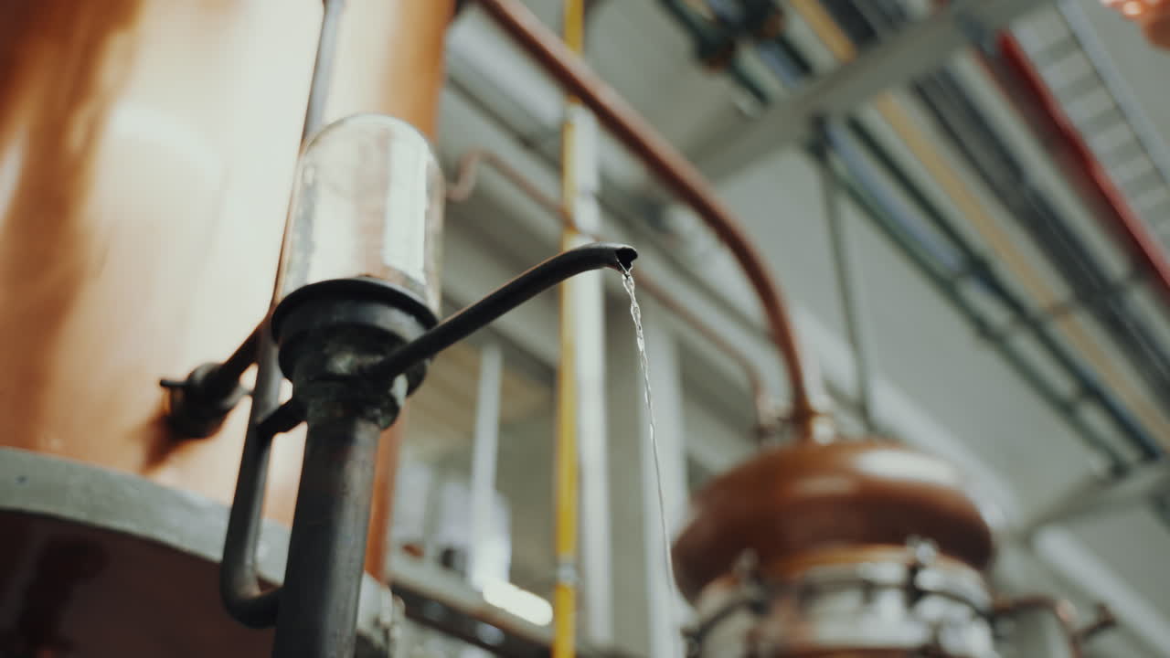 Potret jarak dekat alkohol distilasi yang keluar dari tangki tembaga, proses industri dalam produksi penyulingan gin.
