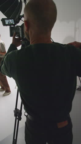 vertical video of male film camera operator shooting movie or video in studio using tripod