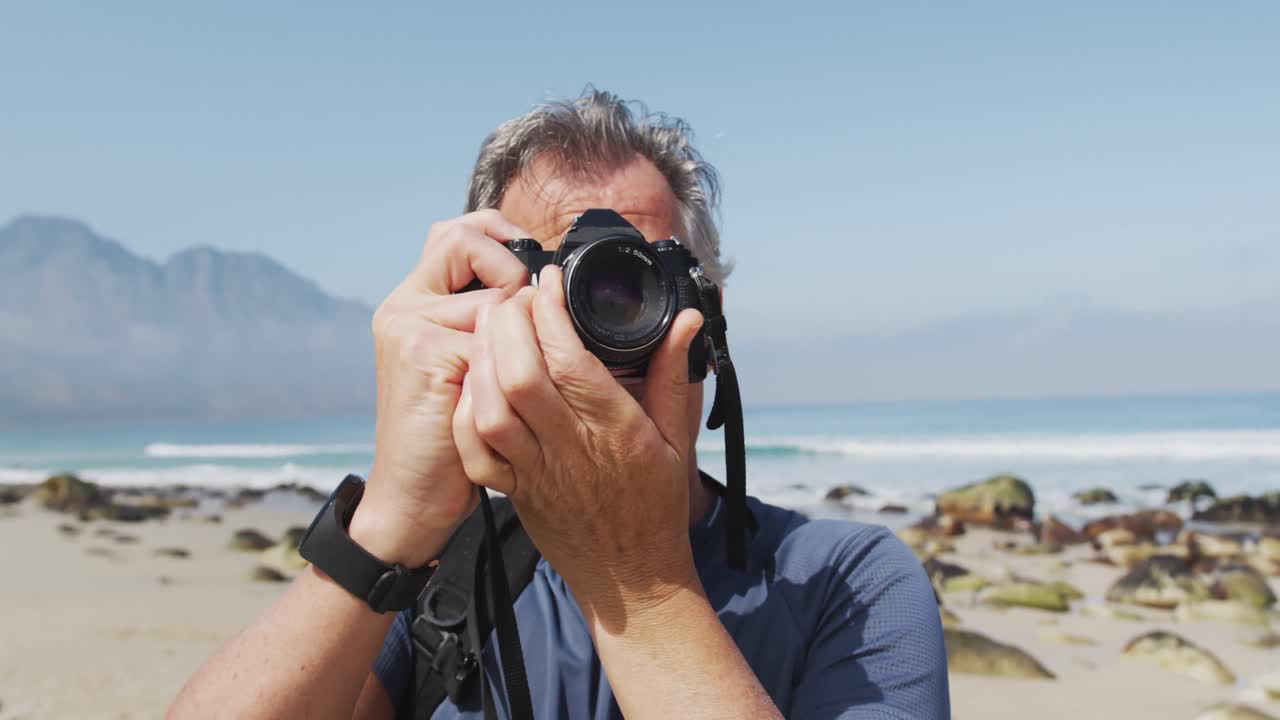 hombre excursionista senior tomando fotos usando una cámara digital en la playa.