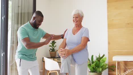 Video-of-happy-african-american-male-physiotherapist-exercising-with-caucasian-senior-woman