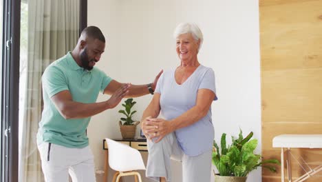 video of happy african american male physiotherapist exercising with caucasian senior woman