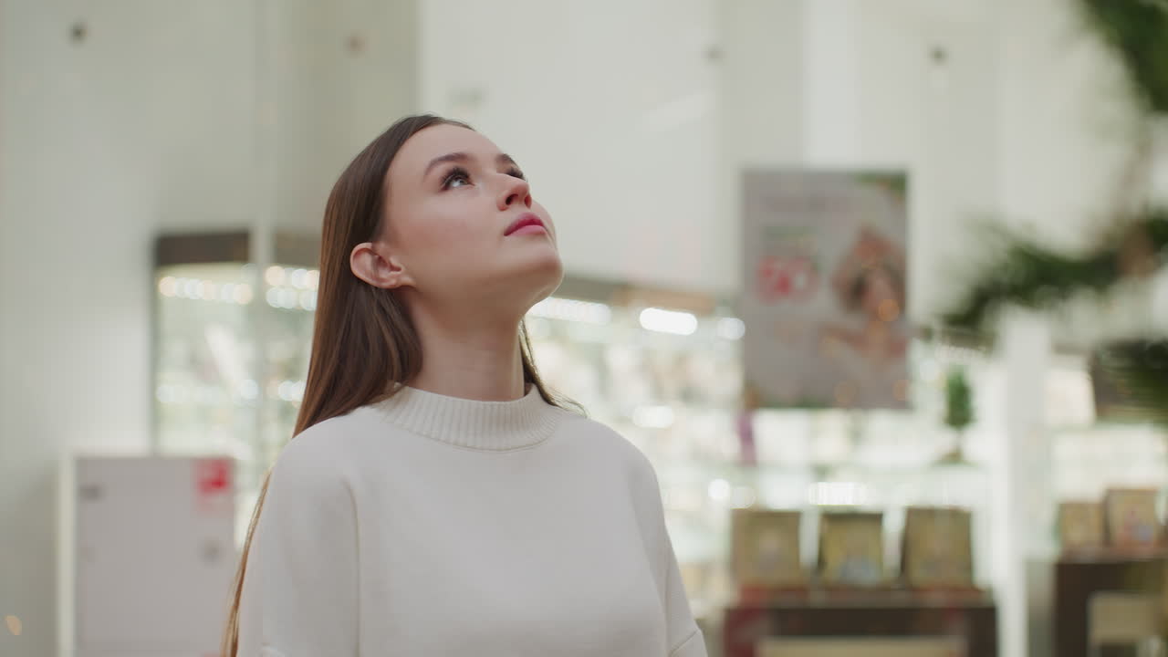 Girl in white walking in modern shopping mall towards decorative Christmas plant, bright lights and retail displays create a vibrant atmosphere, showcasing holiday spirit and festive decor
