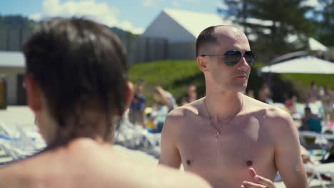 Close-up-Travelling-Dialog-Bald-Italian-man-stands-on-beach-wearing-sunglasses-looks-like-mob