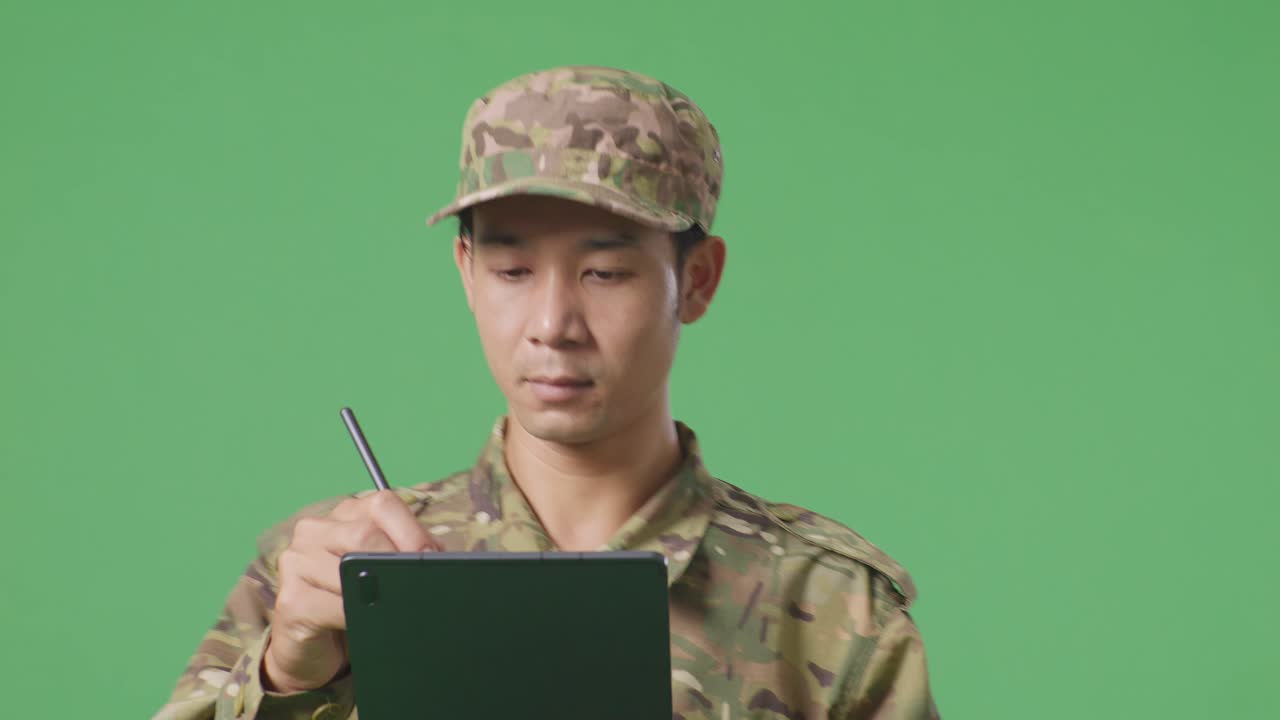 녹색 스크린 배경 스튜디오에서 는 동안 태블릿에 메모를 취하는 아시아 남자 군인의 클로즈업