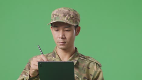 un soldado asiático tomando notas en una tableta mientras camina en el estudio de fondo de la pantalla verde