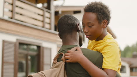 Vista-Trasera-De-Un-Padre-Militar-Sosteniendo-Y-Abrazando-A-Su-Hijo-Fuera-De-Casa-1