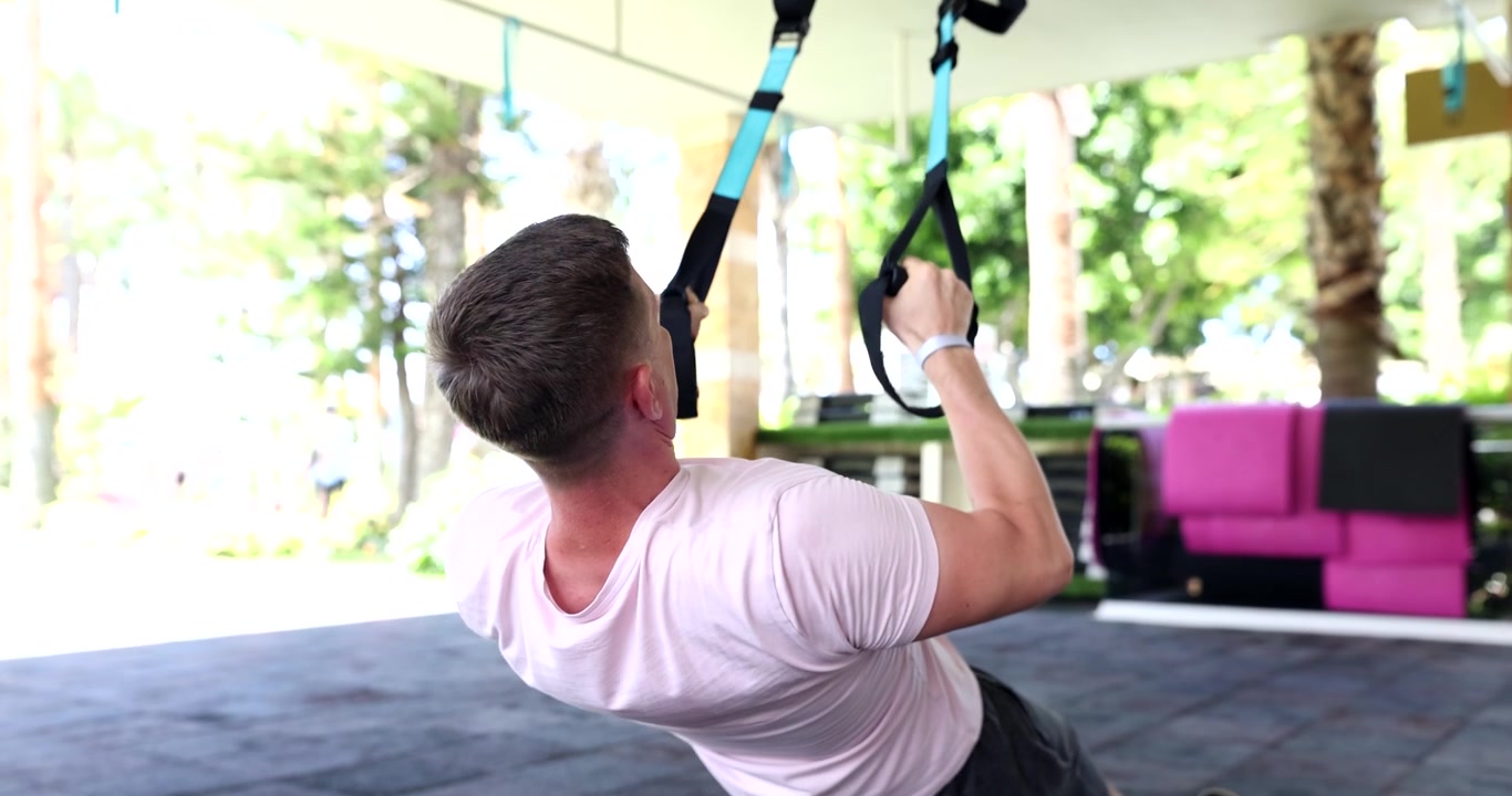 Strong man does pulls up on hanging trx loops in modern gym