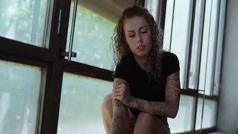 thoughtful tattooed woman looking into the camera and posing in natural light