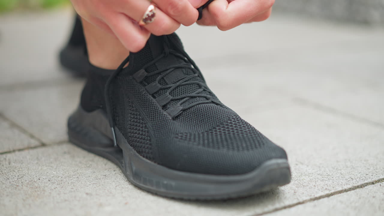 Vista sfocata di una ragazza con scarpe da ginnastica nere che si allaccia le scarpe, l'attenzione è sulle sue scarpe mentre si prepara per una corsa, mostrando uno stile di vita attivo e una routine di fitness.