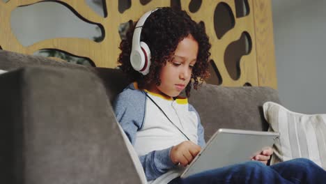 Front-view-of-African-american-boy-with-headset-playing-game-on-digital-tablet-in-lobby-at-hospital-