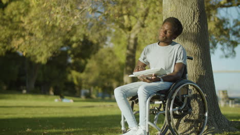 young black man in wheelchair having lunch in city park