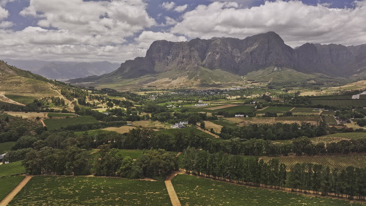Stellenbosch South Africa Aerial v10 flyover a lush valley filled with vineyards, nestled between rolling hills and imposing mountains under a cloudy sky - Shot with Mavic 3 Pro Cine - Jan 6th 2024