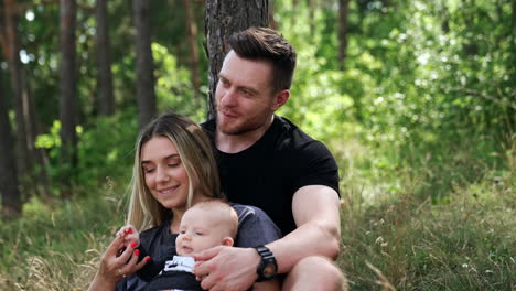happy caucasian couple rest in the forest with their baby. smiling woman holding her child's tiny hand.