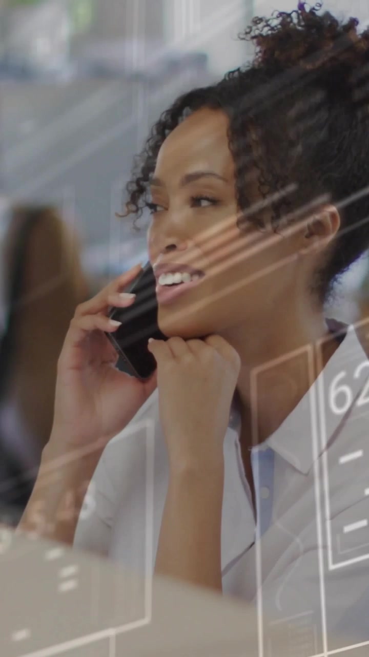 Businesswoman answering smartphone to ear, conducting business call at office with UI overlaying