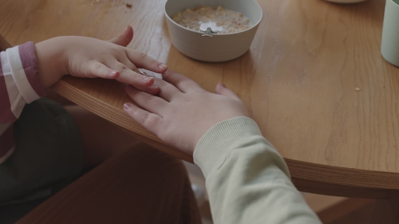 Children Touching Hands at Breakfast Table