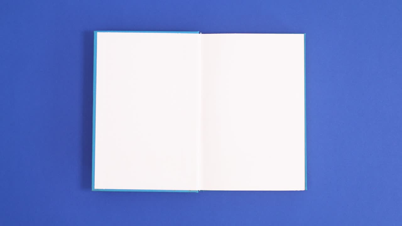 Blue vintage hardcover book appear and open with copy space on blue background. Stop motion flat lay