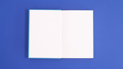 blue vintage hardcover book appear and open with copy space on blue background. stop motion flat lay