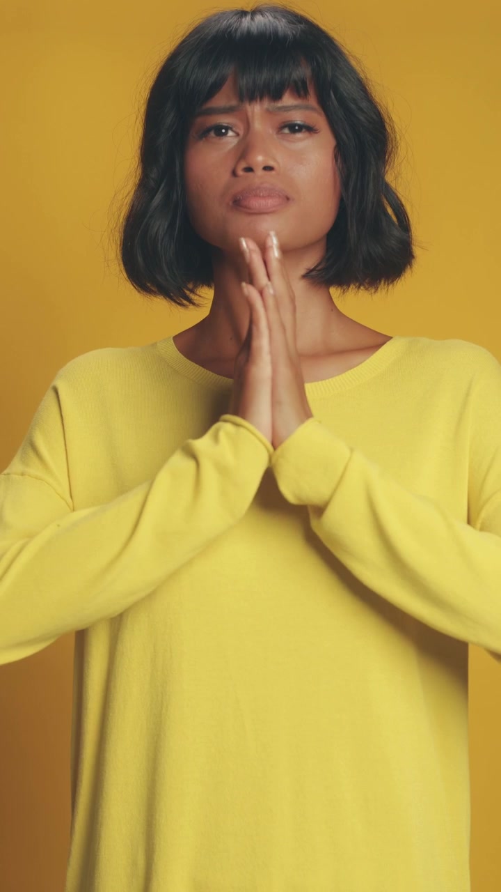 South asian woman in yellow sweater holding hands in prayer pose in calm studio