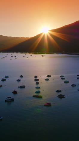 Yachts and boats holding still on the waters of Lake Tahoe, California, USA. Dark mountains silhouettes with setting sun at backdrop. Vertical video