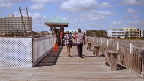 people walk on folly beach pier on sunny day in south carolina