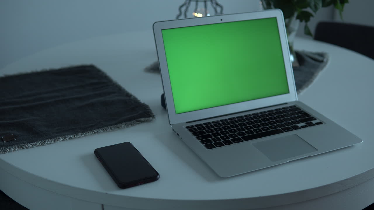 Green screen monitor on laptop and mobile phone, man holds the phone in his hand and puts it in his ear, home office