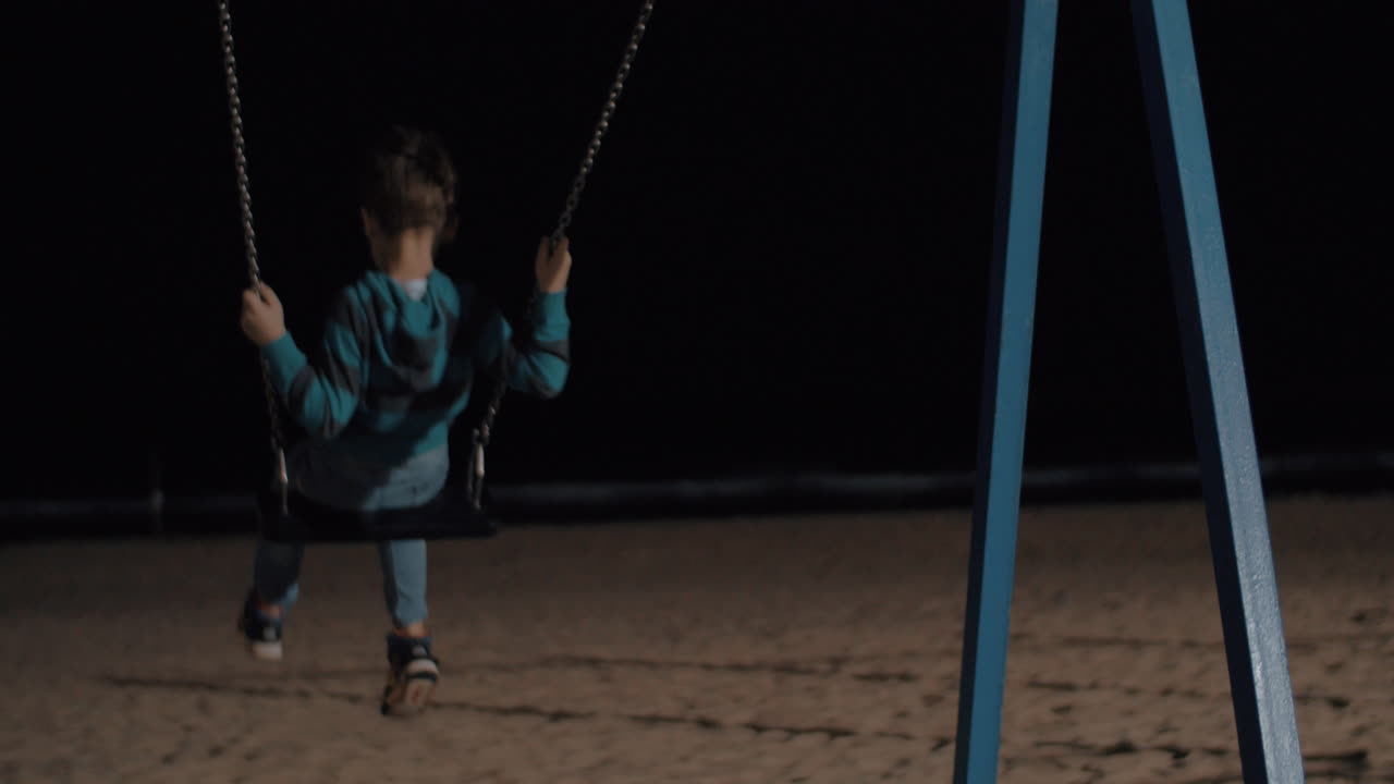 niño balanceándose en la playa por la noche