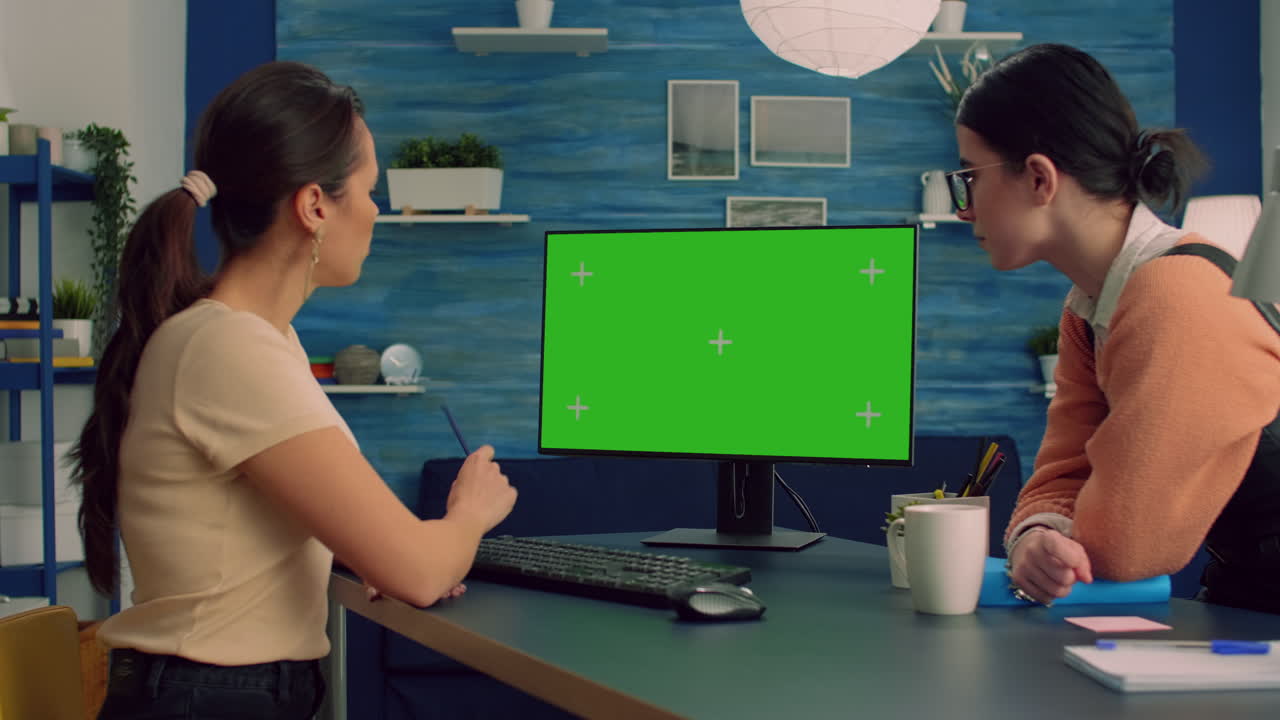 Two collegues working together on computer with mock up green screen chroma key display