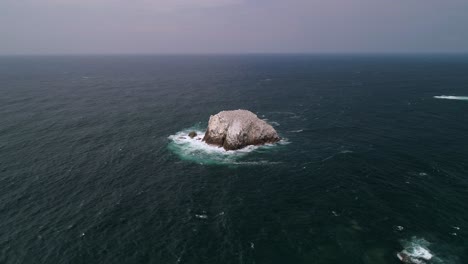 Aerial-drone-shot-of-a-big-rock-formation-known-as-Roca-Blanca-in-Zipolite-beach,-Oaxaca