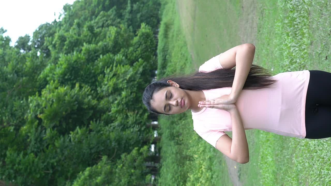 Vertical close-up slow motion shot of a women doing yoga meditation in a green meadow background. Good mood and healthy life concept