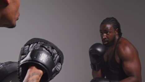 Studio-Shot-Of-Male-Boxer-Sparring-Working-Out-With-Trainer-Wearing-Punch-Mitts-Or-Gloves-Practising-For-Fight-5