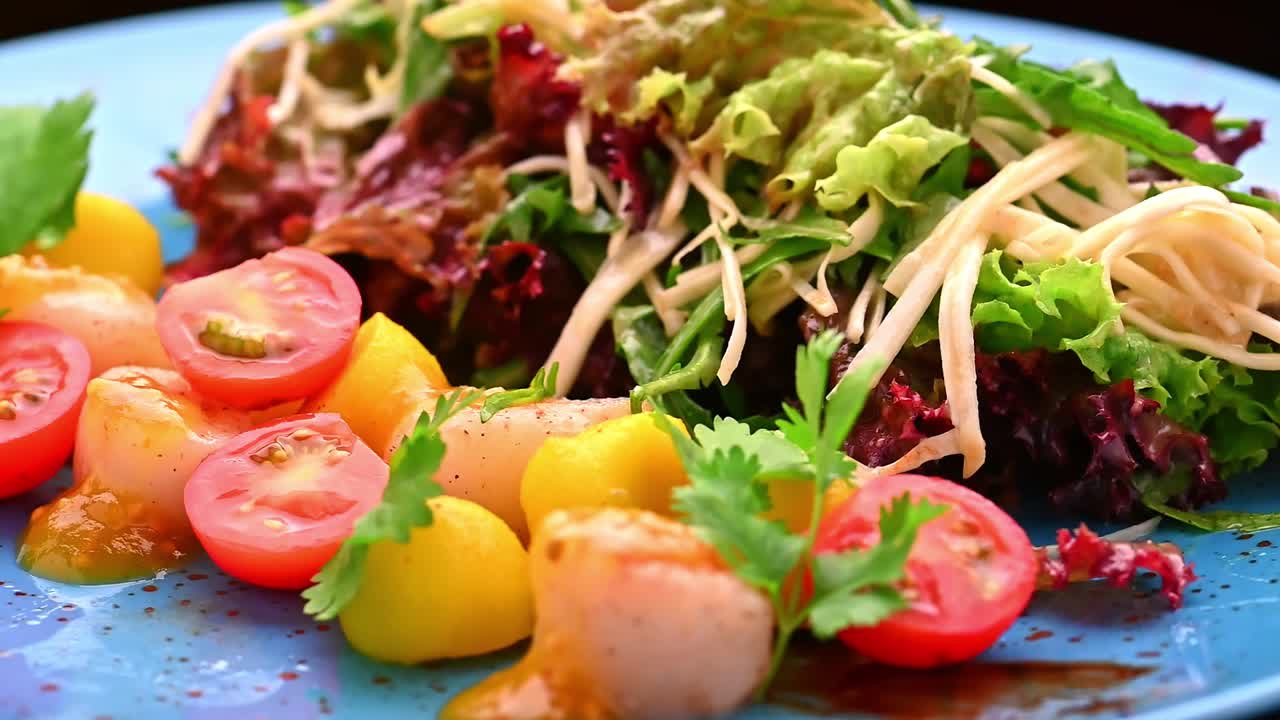 新鮮なサラダが、チェリートマトと野菜とともに青い皿に盛り付けられています。サラダは、さまざまな野菜、チェリートマト、ドレッシングを青い皿に盛り付けて作られています。