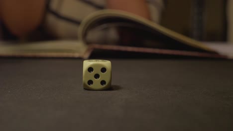 six face dices rolling on black table with role book in background