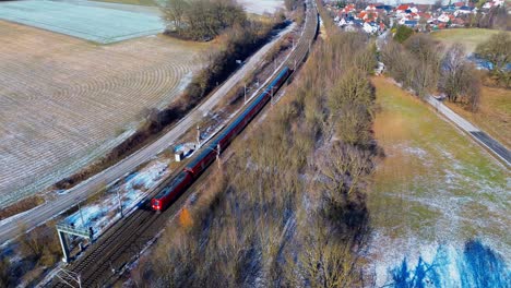 red commuter train navigating through frosty rural landscape