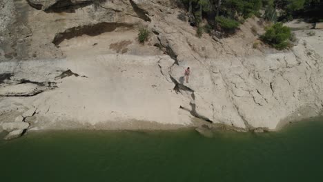 High-Angle-wide-shot-of-man-diving-in-the-lake-from-weathered-rock-in-coastal-area-of-Spain's-national-park