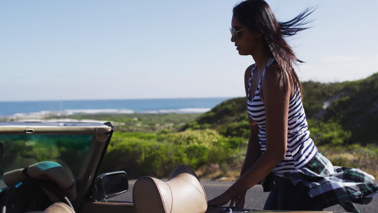 mujer afroamericana con gafas de sol saliendo de un coche descapotable en la carretera