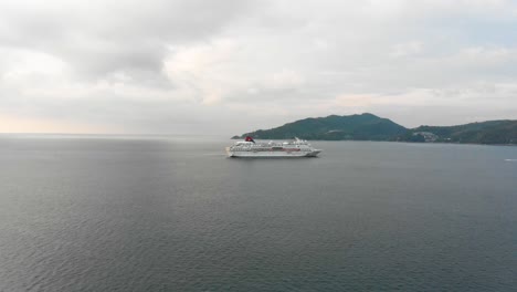 approaching with a steady aerial drone shot of a boat, a speedboat coming from the right side of the frame, and the island in the background at tri trang, phuket in the south of thailand