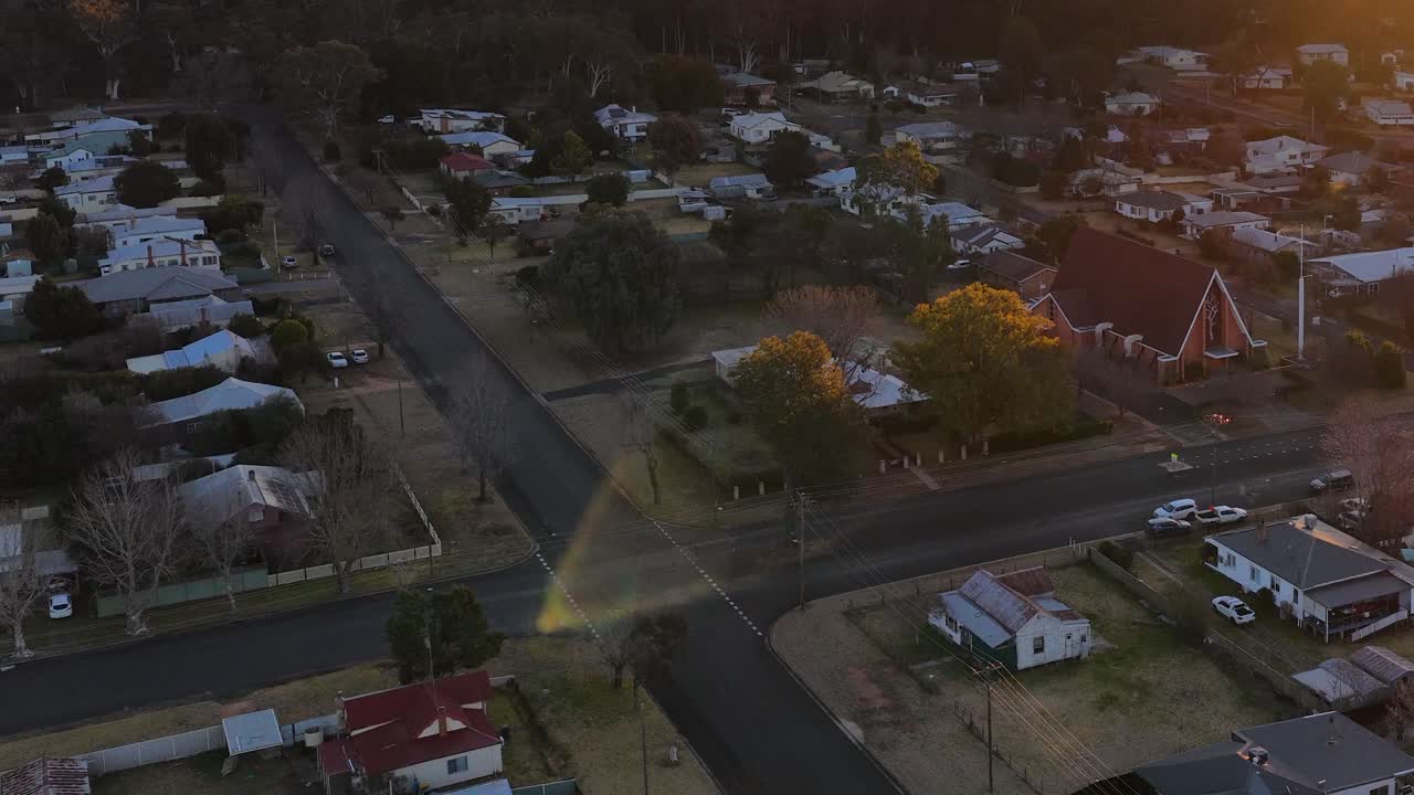 Drone camera glides over suburban homes and streets in Coonabarabran, New South Wales, during golden hour with warm, soft sunlight and gentle movement
