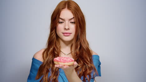 Doubtful-woman-holding-doughnut-indoors.-Girl-trying-not-to-eat-in-studio