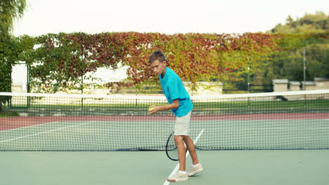 10 代の少年が床にボールを投げ、夏の日の屋外テニスコートでのトレーニング中にラケットで打つ