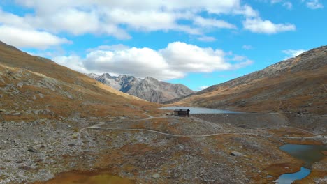 Aerial-View-of-Isolated-Cabin-on-Small-Dam-and-Lake-Under-Swiss-Alps-Mountain-Peaks