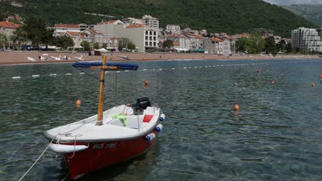 Pequeño-Bote-Atracado-En-Una-Bahía,-Ciudad-Costera-Junto-A-Las-Montañas,-Sur-De-Europa